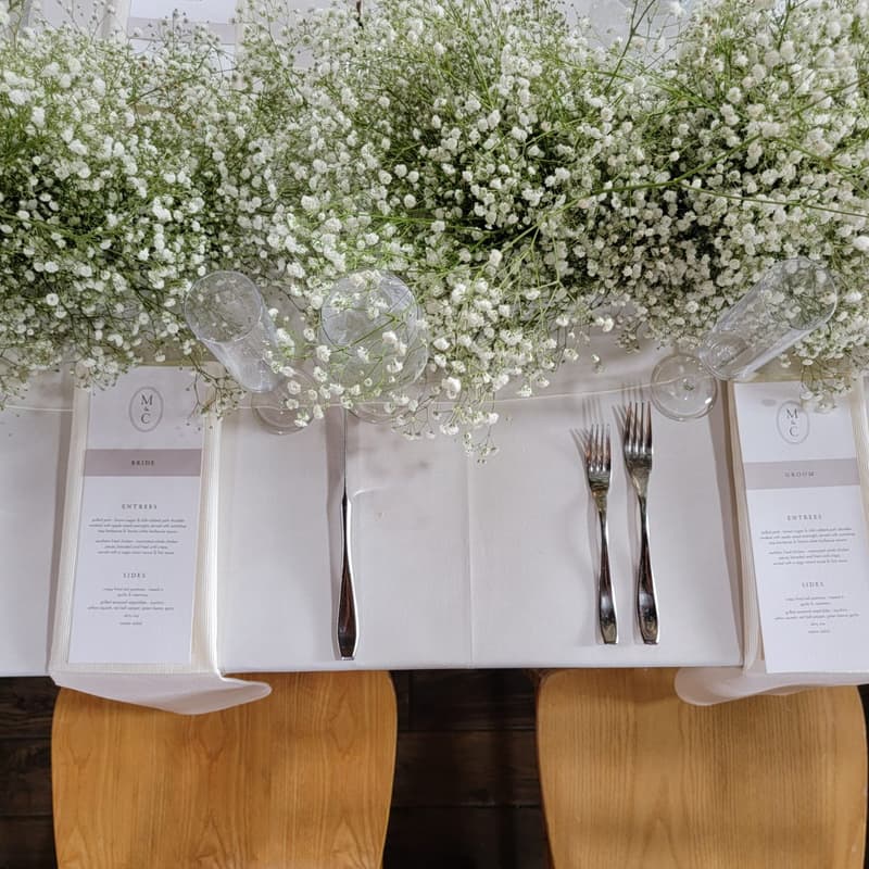 Long table place settings with white linen, menu cards and baby's breath