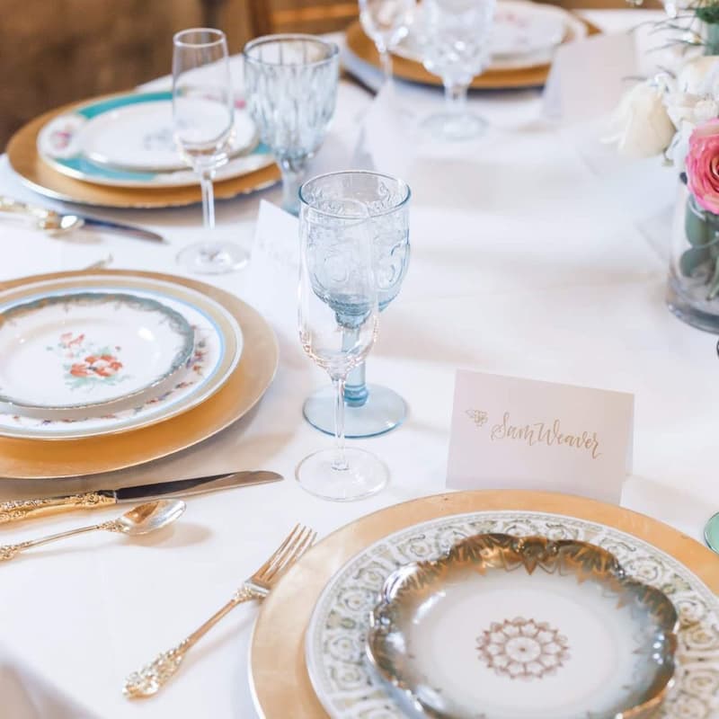 Place setting with a gold charger, vintage china, blue glassware and a calligraphy place card